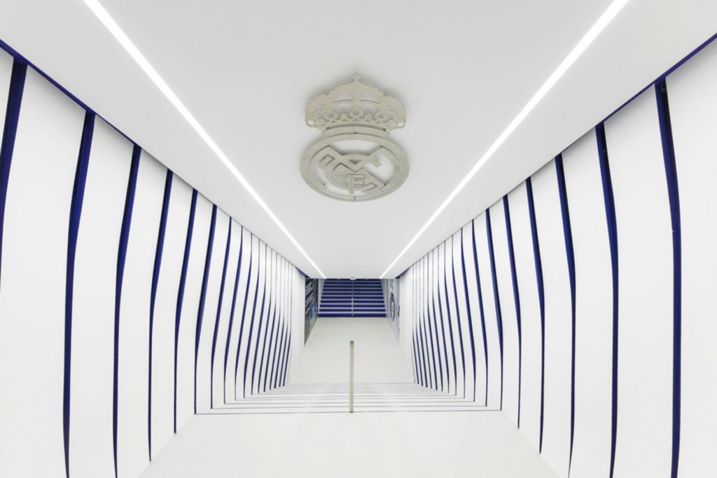 흰색과 파란색 복도에 줄무늬 벽과 천장 엠블럼이 있으며, 멀리 계단으로 이어집니다.