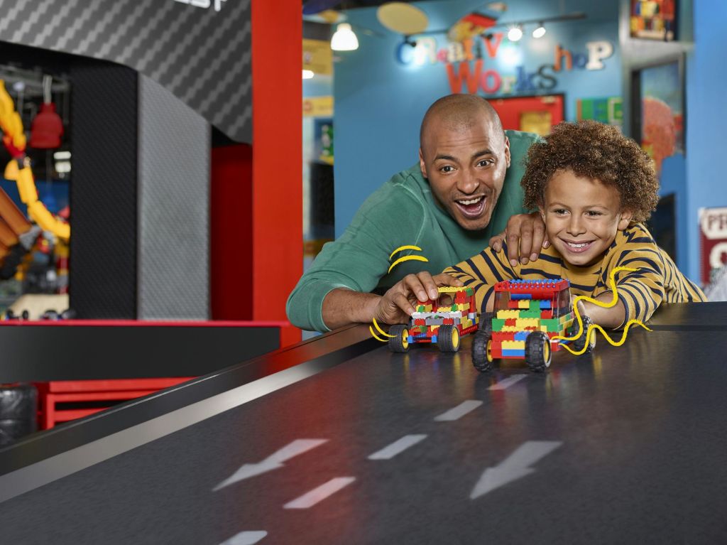 어른과 어린이는 다채로운 색상의 레고 자동차를 타고 트랙을 달리며 미소 짓고 활동에 집중합니다.