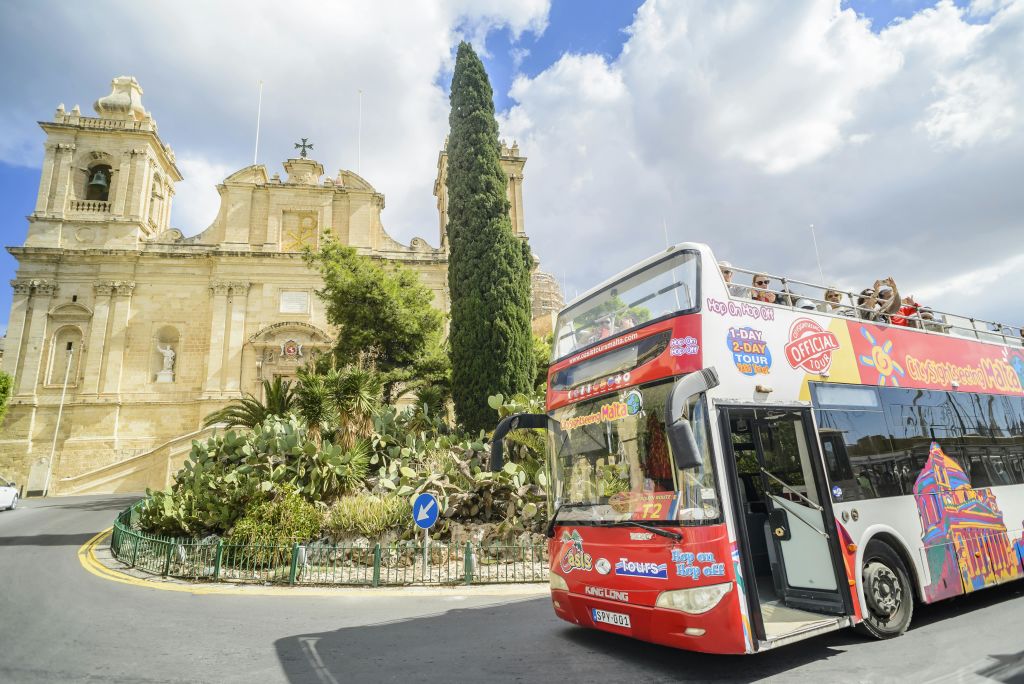 커다란 나무와 녹음이 우거진 역사적인 건물 앞에 빨간색 이층 관광 버스가 있습니다.