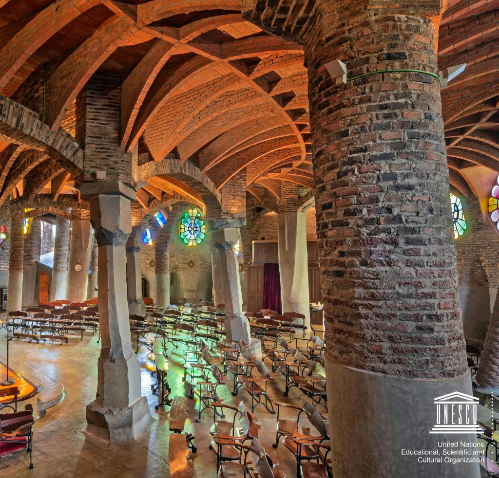 벽돌 기둥, 아치형 천장, 스테인드글라스 창문, 빈 의자가 줄지어 있는 교회 내부. 코너에 유네스코 로고가 있습니다.