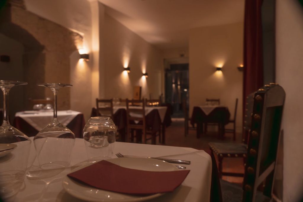 조명이 희미한 레스토랑으로, 전경에는 깔끔하게 세팅된 테이블이 있고, 배경에는 텅 비고 가려진 테이블이 몇 개 있습니다.