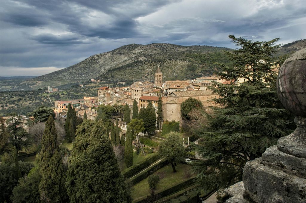 흐린 하늘 아래 나무와 언덕으로 둘러싸인 테라코타 지붕이 있는 유서 깊은 마을입니다.