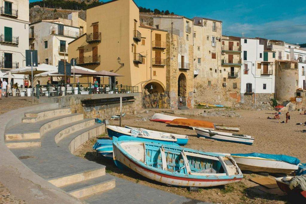 맑고 푸른 하늘 아래 배경으로 오래된 건물과 야외 카페가 있는 모래 해변의 해변 낚시 보트.
