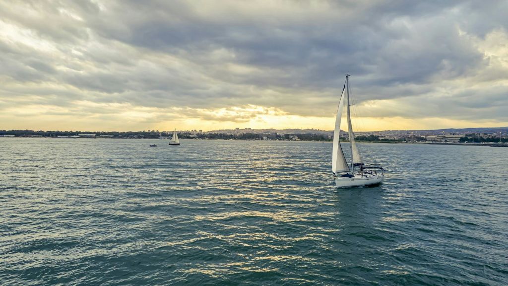 흐린 하늘 아래 잔잔한 물줄기에 돛단배 두 척이 있고, 저 멀리 해안선이 배경으로 보입니다.