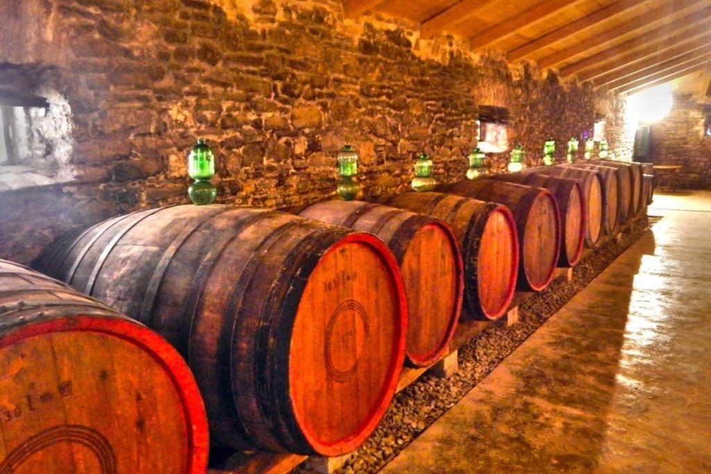 석조 벽에 나무 통이 줄지어 늘어선 조명이 희미한 지하실에 각각 녹색 유리병이 놓여 있습니다.