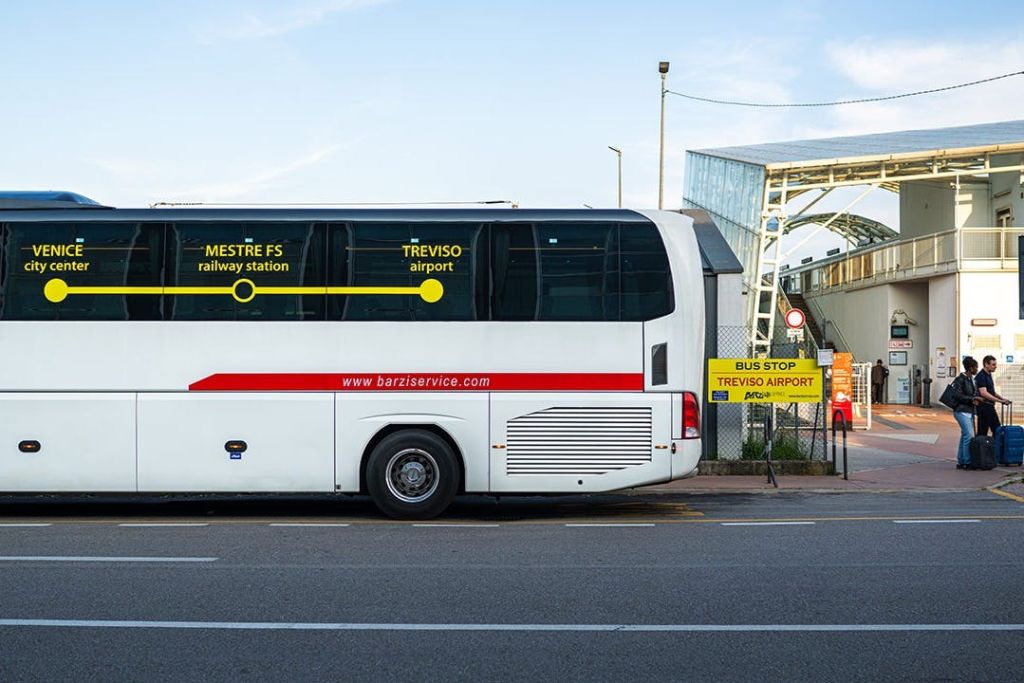 노란색 표지판이 있는 버스 정류장에 "메스트레 FS 기차역" 과 "트레비소 공항" 목적지가 있는 흰색 버스가 주차되어 있습니다.