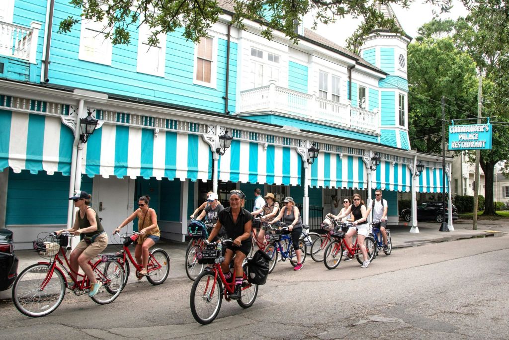 화창한 날 줄무늬 천막이 있는 밝은 파란색 건물을 지나 자전거를 타는 사람들입니다.