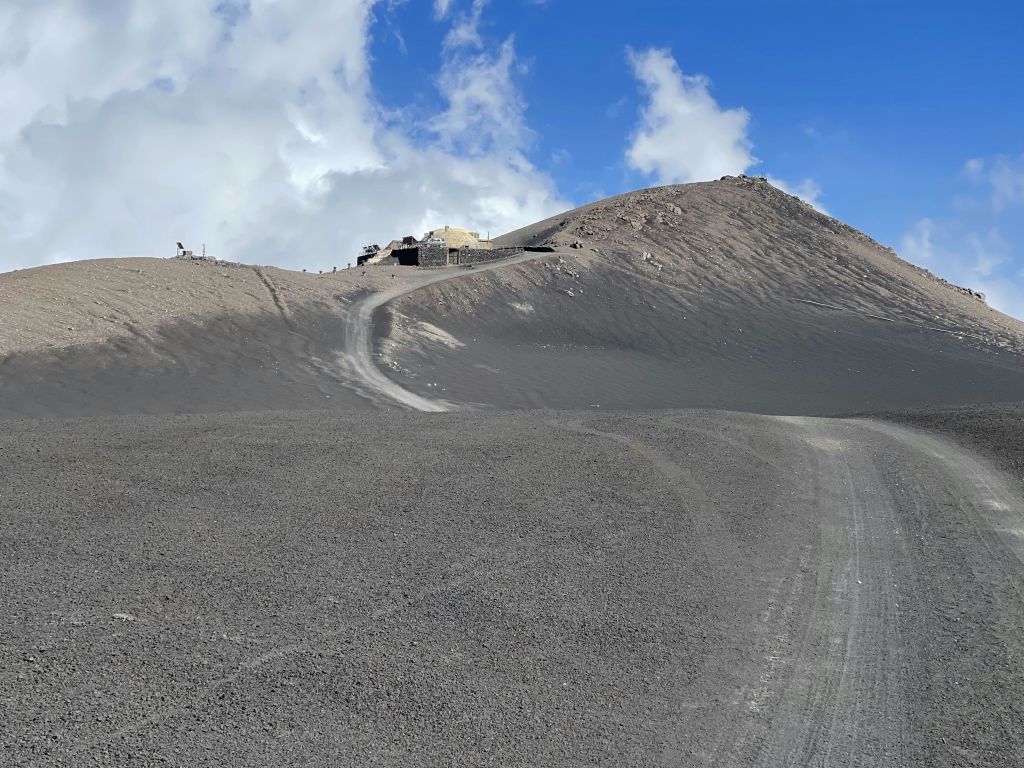 험준하고 구불구불한 흙길은 구름이 흩날리는 푸른 하늘 아래 황량하고 바위가 많은 경사면 꼭대기에 있는 건물로 이어집니다.