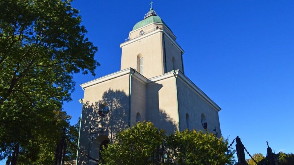 푸른 하늘 아래 나무로 둘러싸인 녹색 돔과 십자가가 있는 높은 베이지색 교회입니다.