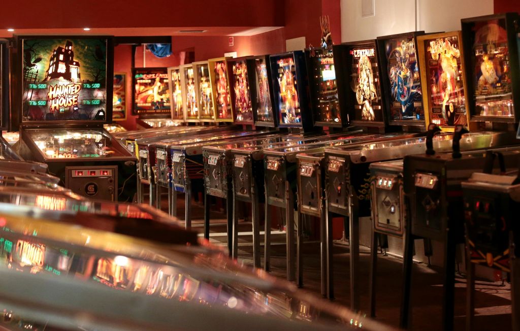 다채롭고 빛나는 백보드가 있는 희미한 조명의 아케이드에 핀볼 기계가 줄지어 있습니다.