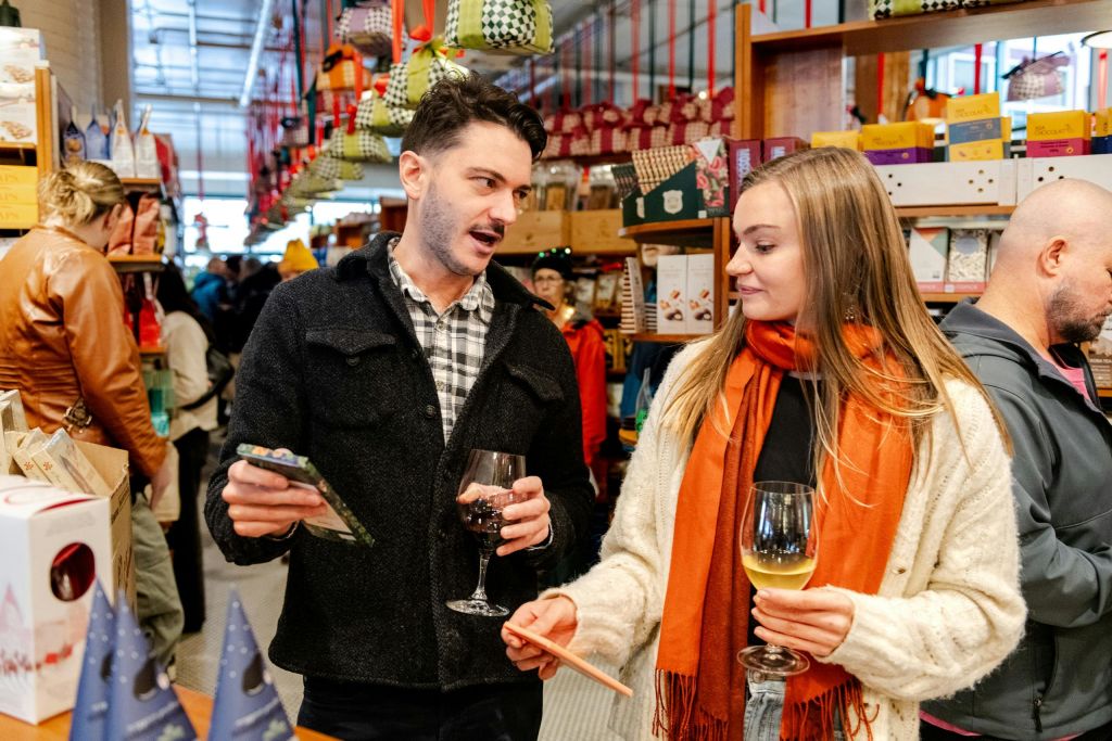 와인잔을 들고 있는 두 사람이 다양한 물품이 가득한 진열대와 진열대가 있는 번잡한 매장에서 이야기를 나누고 있습니다.