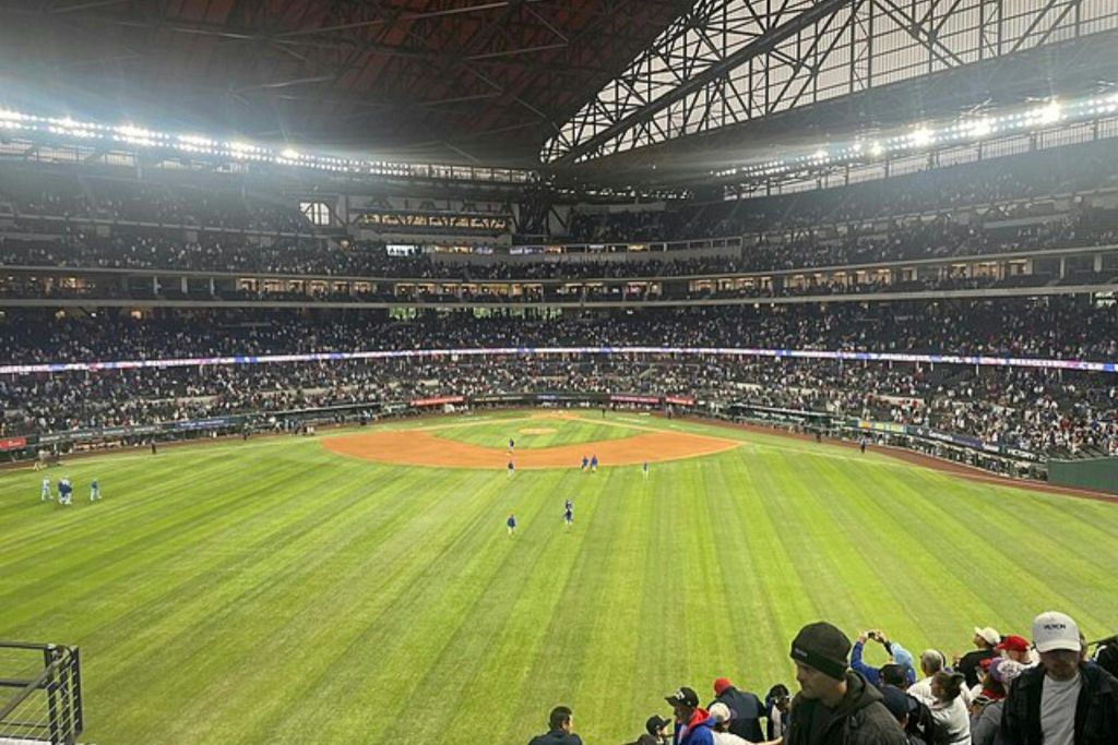 녹색 필드와 선수들이 있는 야구 경기장은 지붕 아래 큰 군중으로 둘러싸여 있습니다.