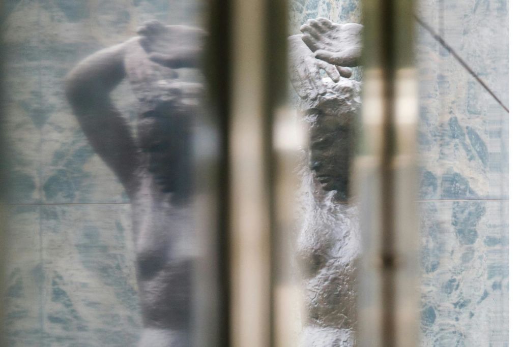반사되고 왜곡된 표면을 통해 보이는 팔을 들어 올린 사람의 동상이 흐릿하게 보입니다.