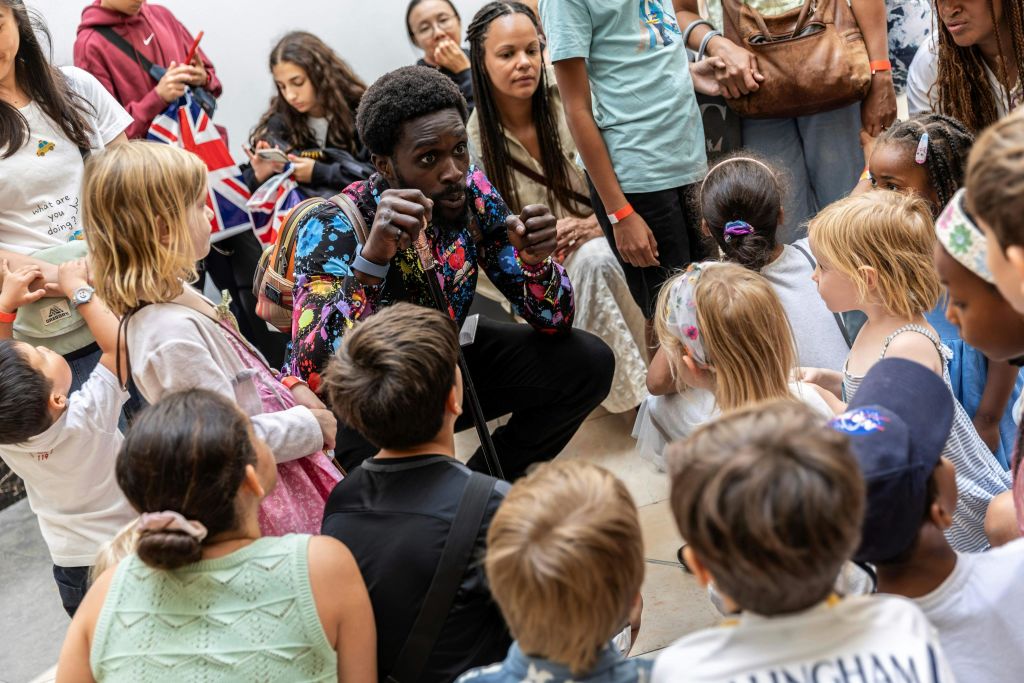 한 남자가 실내에 모여 있는 아이들과 어른들을 향해 애니메이션처럼 이야기하고 있습니다.