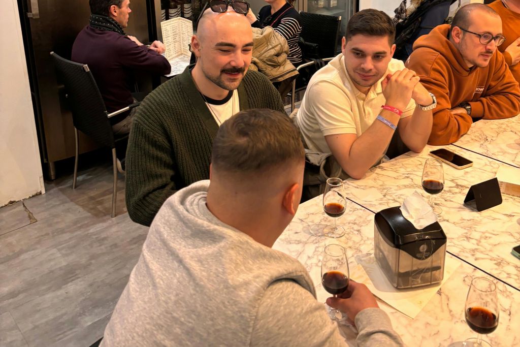 음료수, 티슈 디스펜서, 전화기가 놓인 대리석 테이블에 둘러앉은 네 명의 남성이 카페에서 대화를 나누고 있습니다.