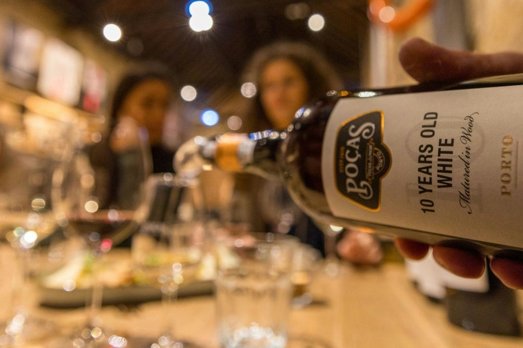 음식이 담긴 식탁의 유리잔에 와인 한 병이 쏟아졌고, 두 사람이 뒤에서 흐릿하게 보였다.