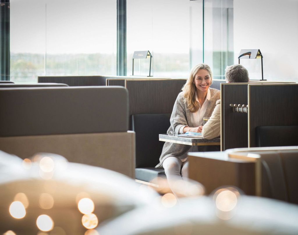 한 여성과 한 남성이 현대적인 카페 부스에 앉아 미소를 짓고 이야기를 나누고 있으며, 파티션 뒤에는 전등이 켜져 있습니다.