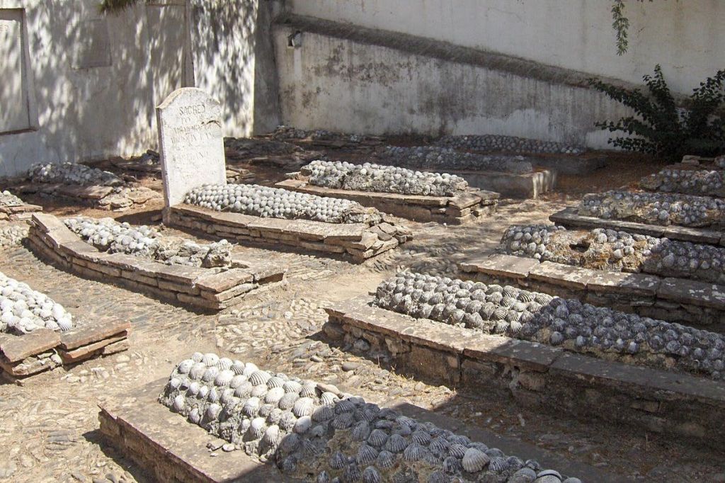 흰색 벽을 배경으로 오래된 공동묘지에 조개껍질로 덮인 비석이 있는 무덤이 몇 개 있습니다.