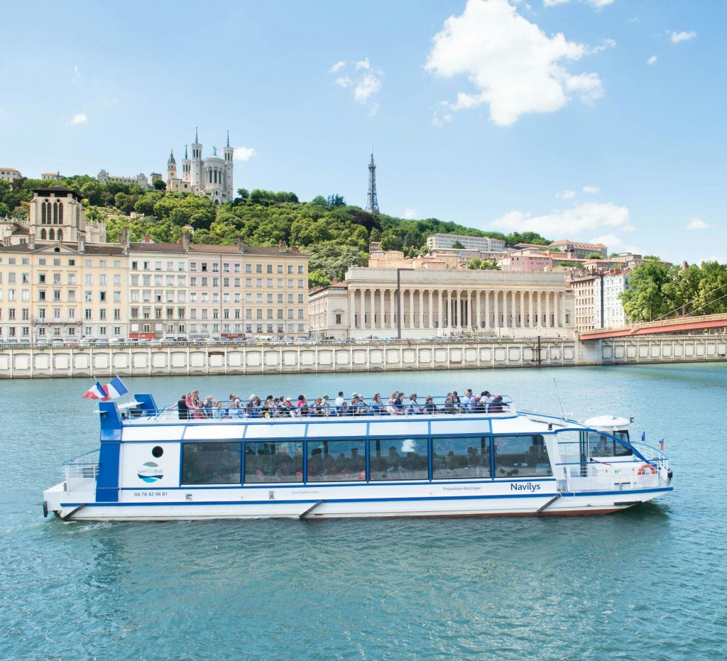 맑은 날 언덕을 배경으로 역사적인 건물과 바실리카가 있는 강가에 탁 트인 정상 갑판이 있는 관광 보트.