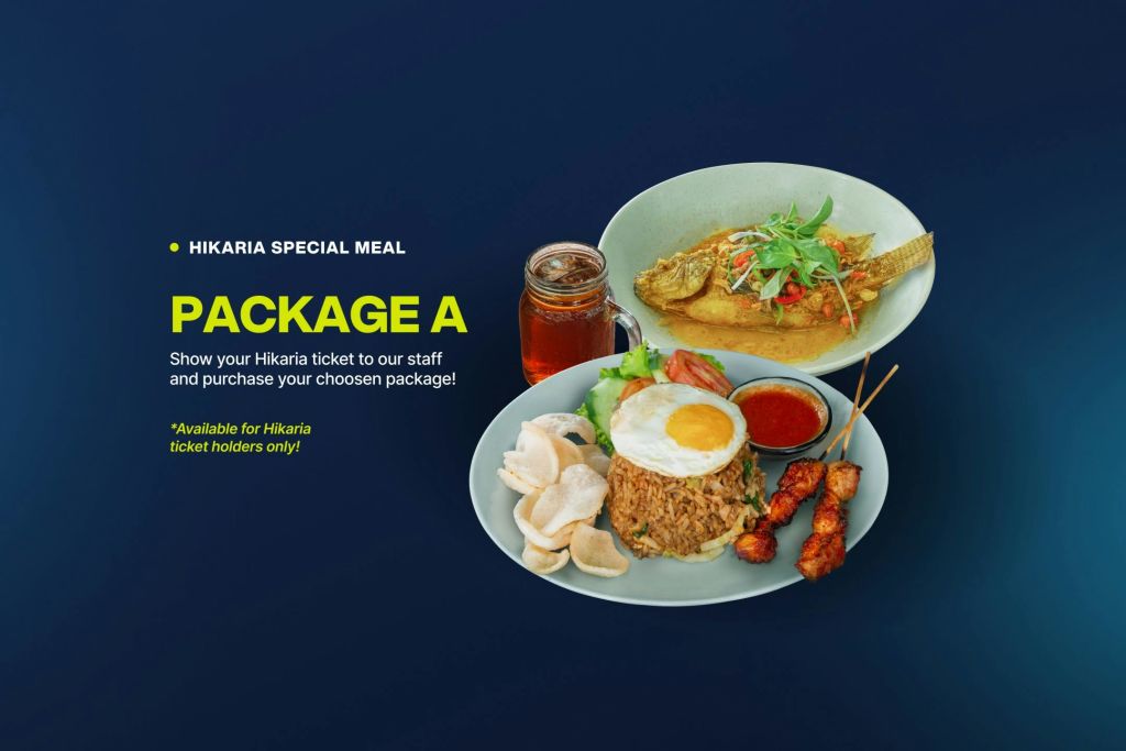 볶음밥, 계란, 사테 꼬치, 크래커가 담긴 접시가 생선구이가 담긴 두 번째 접시 옆에 있습니다. 둘 다 아이스티를 곁들입니다. "Hikaria Special Meal Package A" 라는 문구가 적혀 있습니다.