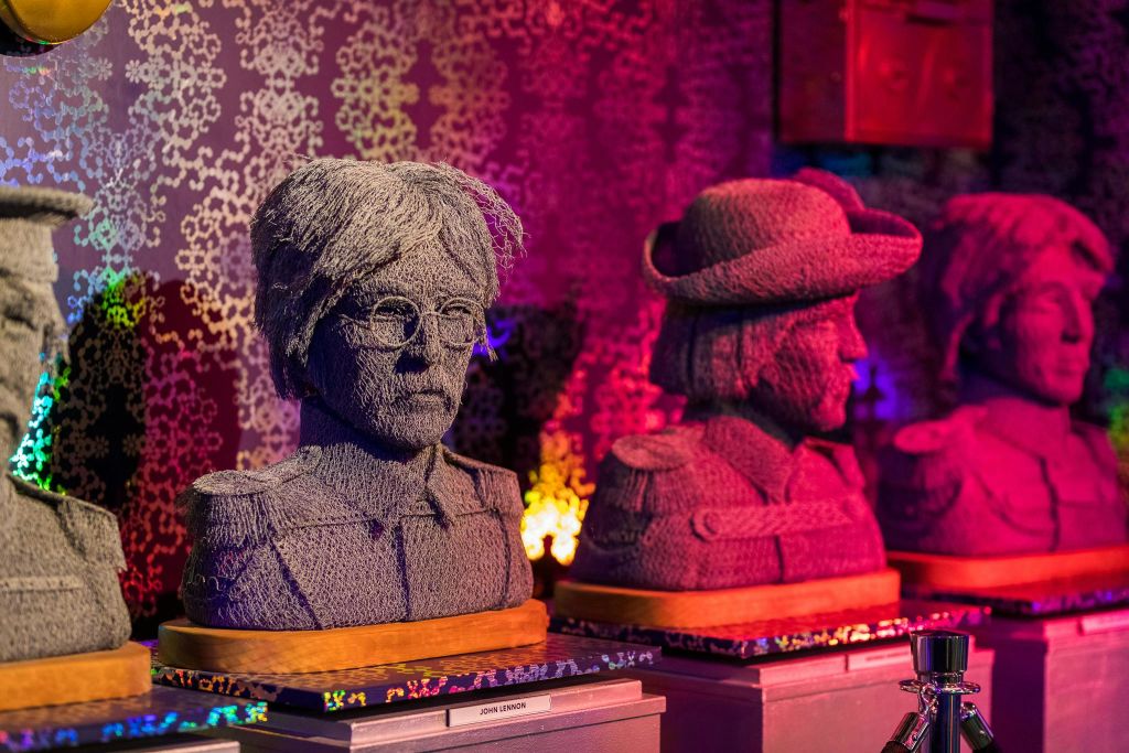 회색 원사로 만든 가슴 두 개, 하나는 안경을 쓰고 다른 하나는 모자를 쓰고 화려한 무늬가 있는 방의 받침대에 전시되어 있습니다.