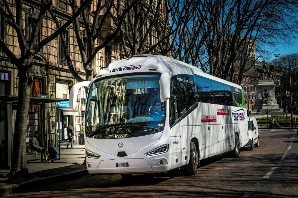 건물과 잎이 없는 나무가 늘어선 도시 거리에 흰색 테라비전 버스가 주차되어 있습니다.