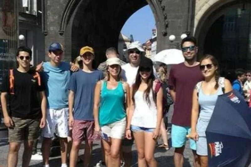 화창한 날 석조 아치길 앞에 서서 웃고 있는 사람들의 일행. 어떤 사람들은 우산을 들고 여름 옷을 입습니다.