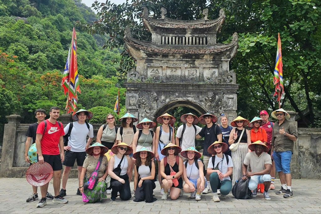 녹음으로 둘러싸인 화려한 석조 문 앞에서 원뿔 모양 모자를 쓴 사람들이 포즈를 취하고 있습니다.