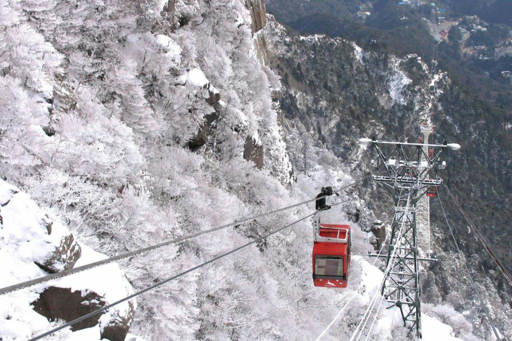 붉은 케이블카가 하얀 눈으로 뒤덮인 빽빽한 나무가 눈 덮인 산악 지대를 통과합니다.