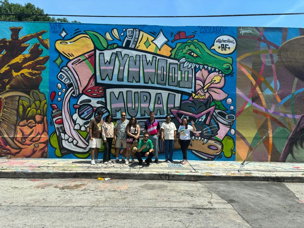 다채로운 벽화 앞에서 '윈우드 벽화' 라는 글과 다양한 생동감 넘치는 일러스트레이션으로 포즈를 취하고 있는 사람들.