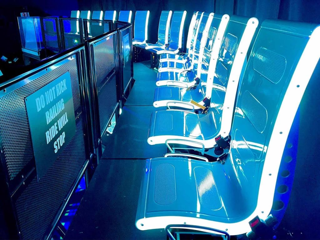 근처에 검은색 난간이 있는 파란색 좌석이 줄지어 있으며, "난간을 걷어차지 마세요. 라이딩이 중단됩니다." 라는 문구가 적힌 표지판이 있습니다.