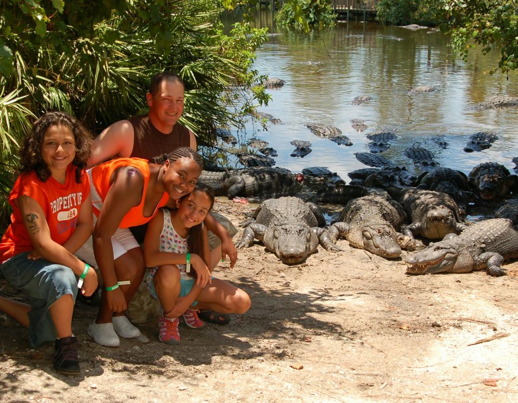 수많은 악어가 울창한 초목과 물을 배경으로 연못 근처에서 포즈를 취하는 네 사람.