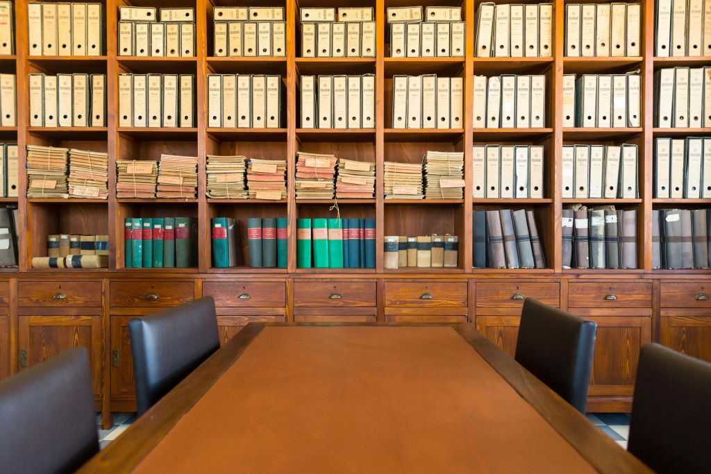 검은색 의자 두 개가 놓인 회의용 탁자 뒤에 바인더, 책, 파일로 가득 찬 나무 선반이 있습니다.