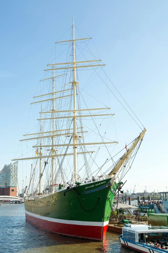 항구에 정박한 커다란 초록색과 흰색의 항해선에는 인근을 거닐고 있는 사람들과 현대적인 건물이 배경을 이루고 있습니다.