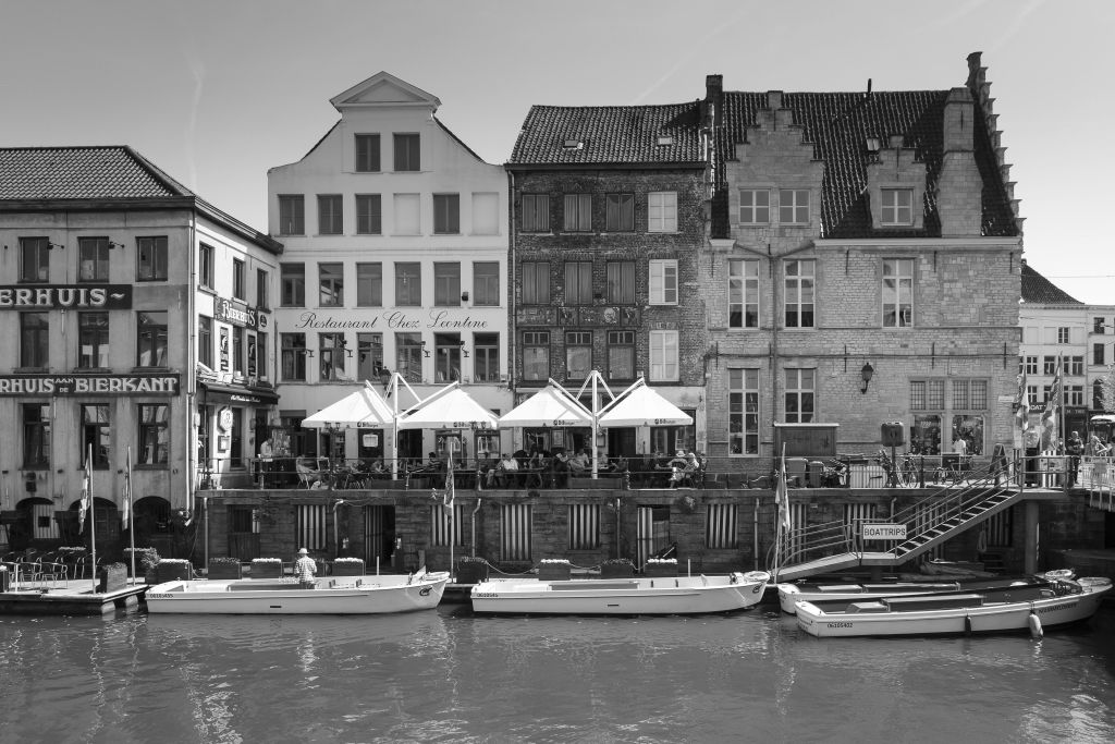 오래된 건물 앞에 보트가 있고 야외 좌석이 있는 레스토랑이 있는 운하의 흑백 사진.