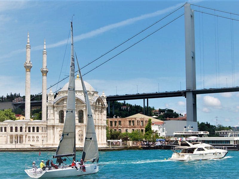 모스크, 건물, 현수교를 배경으로 맑고 푸른 하늘 아래 청록색 바다에서 요트를 즐겨보세요.