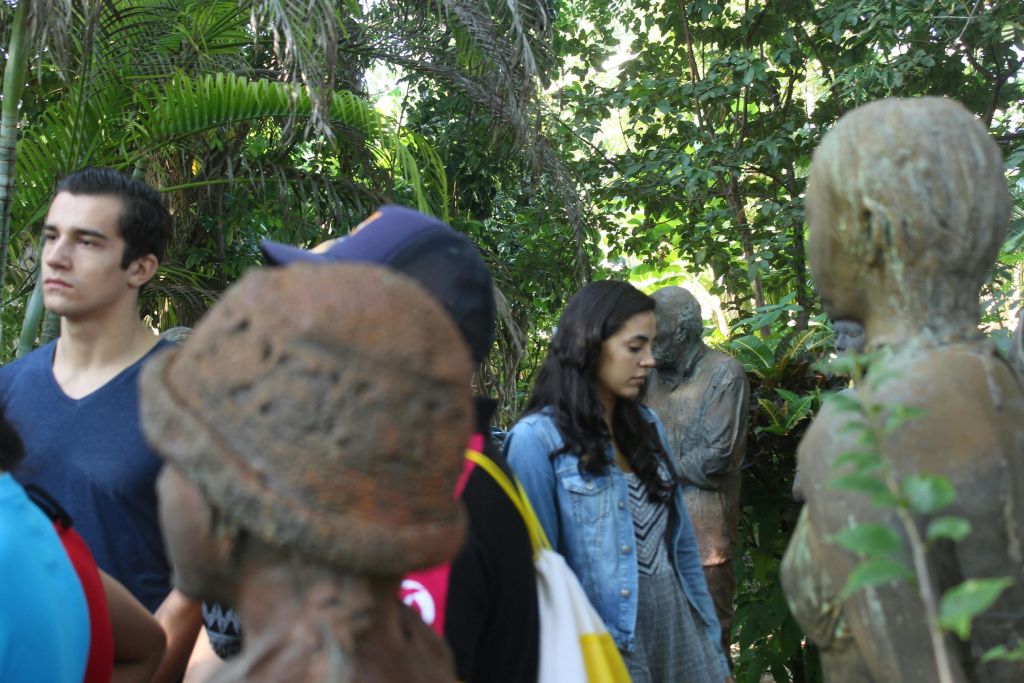열대 단풍이 우거진 녹음이 우거진 야외 공간에 서 있는 사람들 (앞쪽에 모자를 쓴 사람 포함).