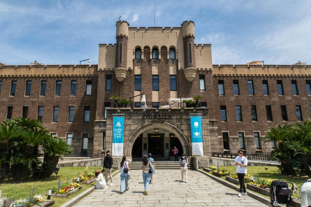 중앙의 아치형 출입구, 현수막, 잘 손질된 잔디밭이 있는 크고 유서 깊은 벽돌 건물 앞을 사람들이 거닐고 있습니다.