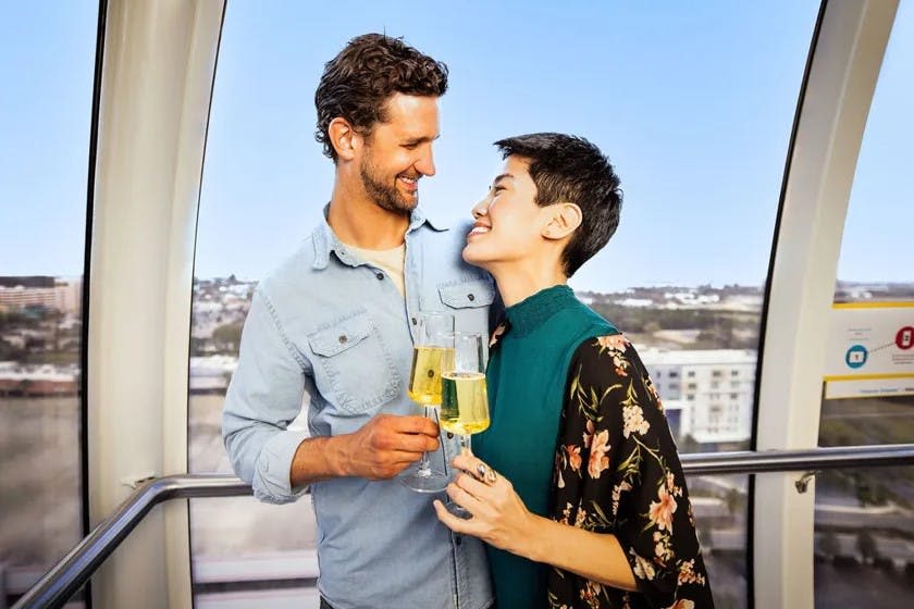 도시 풍경 배경 앞에 가까이 서서 샴페인 잔을 들고 건배하는 미소 짓는 커플.