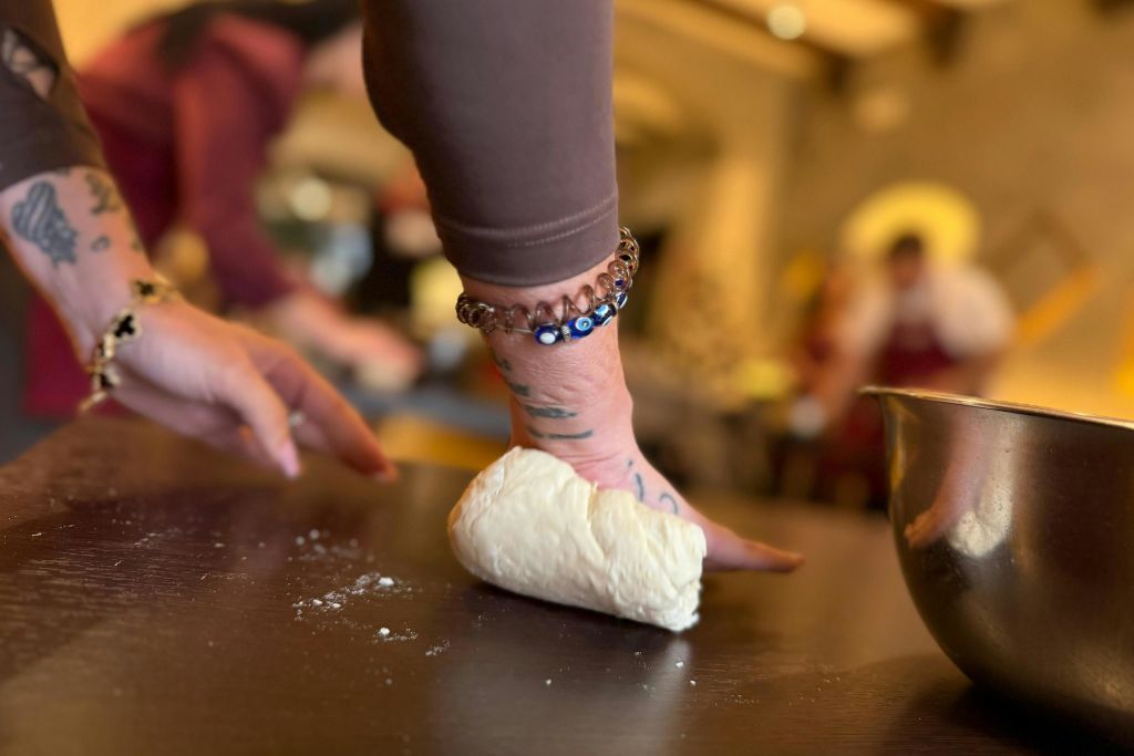 흐릿한 주방 환경에서 어두운 표면에 반죽을 반죽하고 손목에 팔찌가 보입니다.