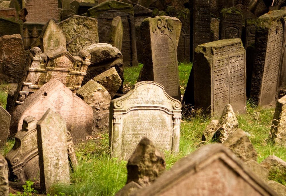 다양한 모양과 크기의 풍화된 묘비가 오래된 공동묘지의 잔디가 우거진 가운데 서 있습니다.