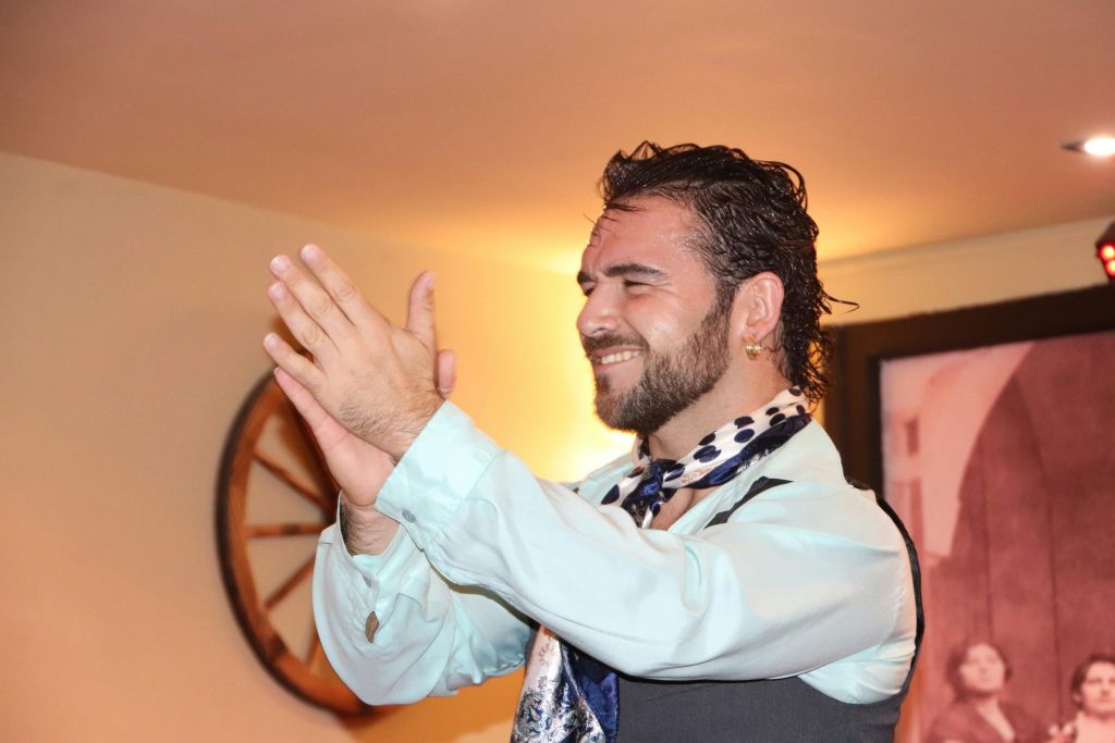 조끼와 스카프를 두른 젖은 머리의 남성이 실내에서 눈을 감은 채 박수를 치고 있습니다.