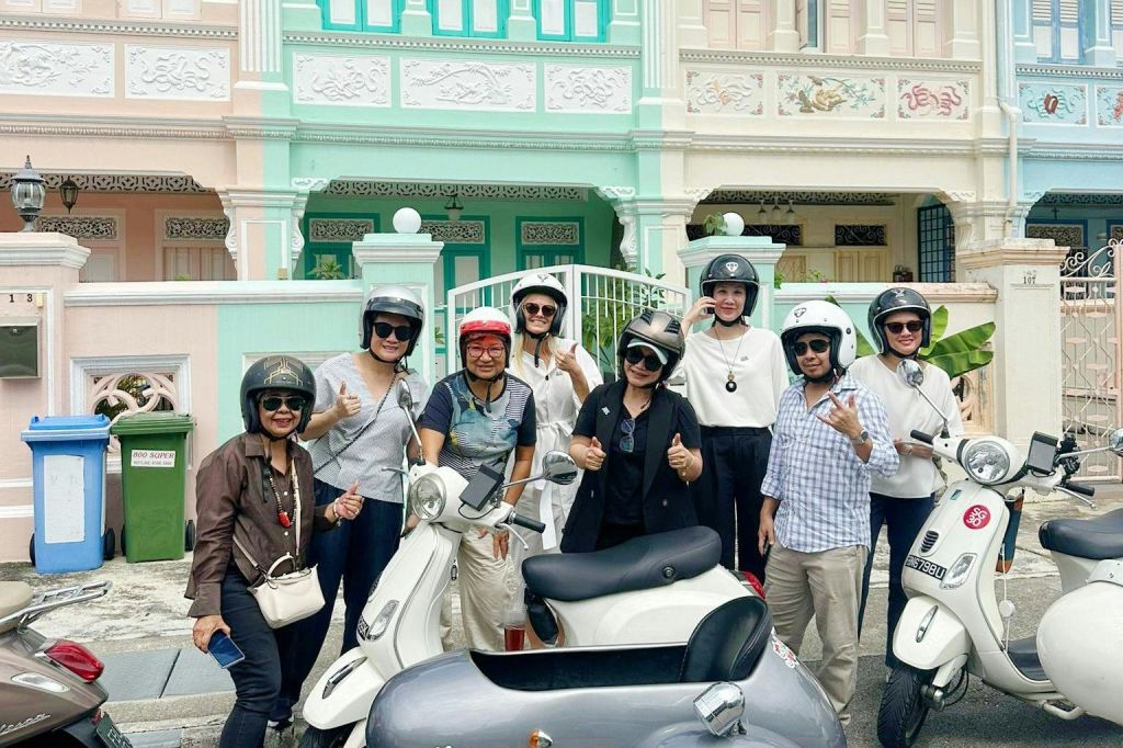 화려한 외관이 돋보이는 화려한 건물 앞에서 헬멧을 쓴 사람들이 스쿠터와 함께 포즈를 취하고 있습니다.