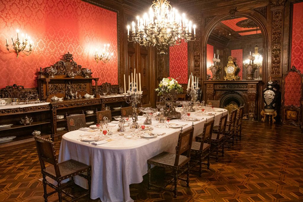 하이백 의자, 샹들리에, 풍부한 장식 요소로 둘러싸인 식사용 긴 테이블이 있는 화려한 다이닝 룸입니다.