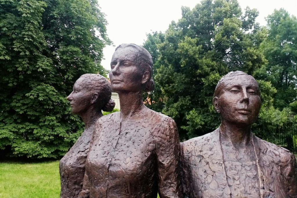 정장 차림의 여성 동상 세 개가 무성한 푸른 나무를 배경으로 야외에 전시되어 있습니다.