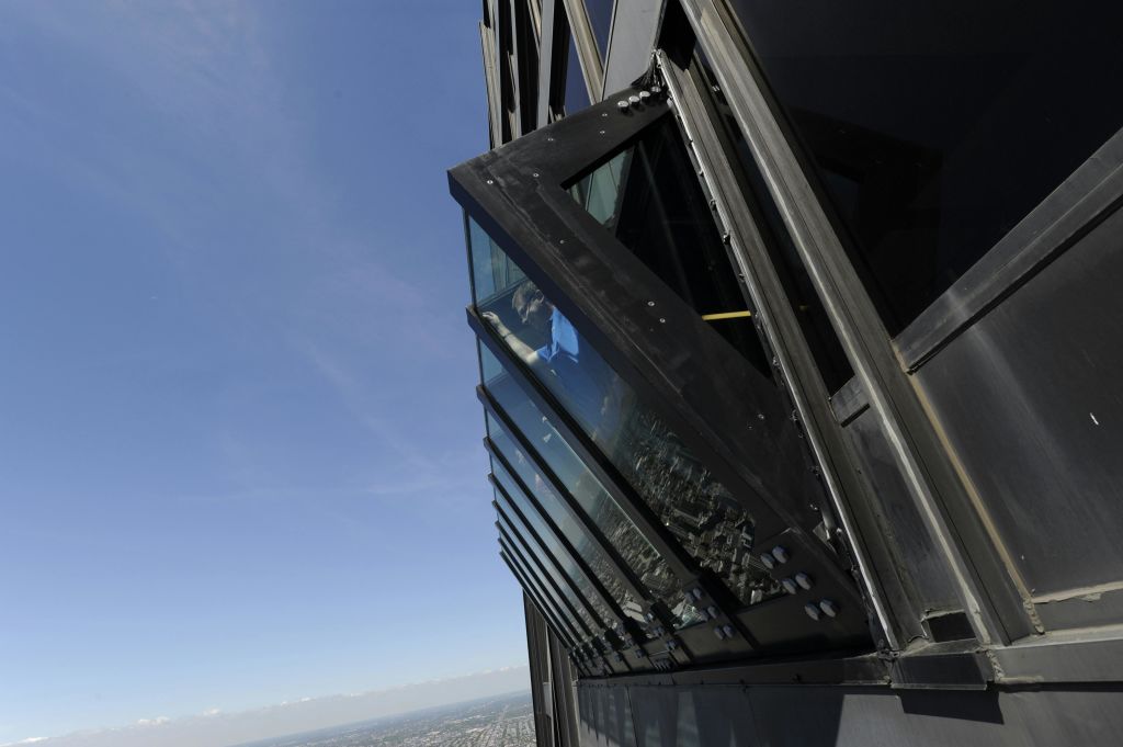 한 사람이 도시 경관 위로 기울어진 유리 창문 상자를 배경으로 맑고 푸른 하늘을 배경으로 서 있습니다.