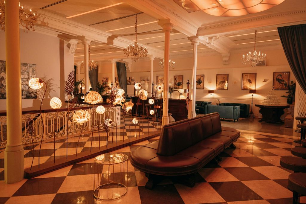 체크무늬 바닥, 가죽 좌석, 샹들리에 조명, 벽에 장식된 액자 예술품을 갖춘 우아한 라운지로 장식된 램프가 조명을 비춥니다.