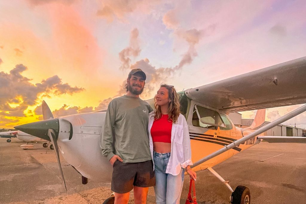 석양이 질 무렵 작은 비행기 앞에는 따뜻한 빛과 구름이 가득한 미소 짓는 커플이 서 있습니다.