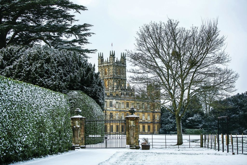 서리가 내린 나무와 창백한 겨울 하늘 아래 울타리로 둘러싸인 철문 뒤에 높이 솟은 첨탑이 있는 눈 덮인 성.