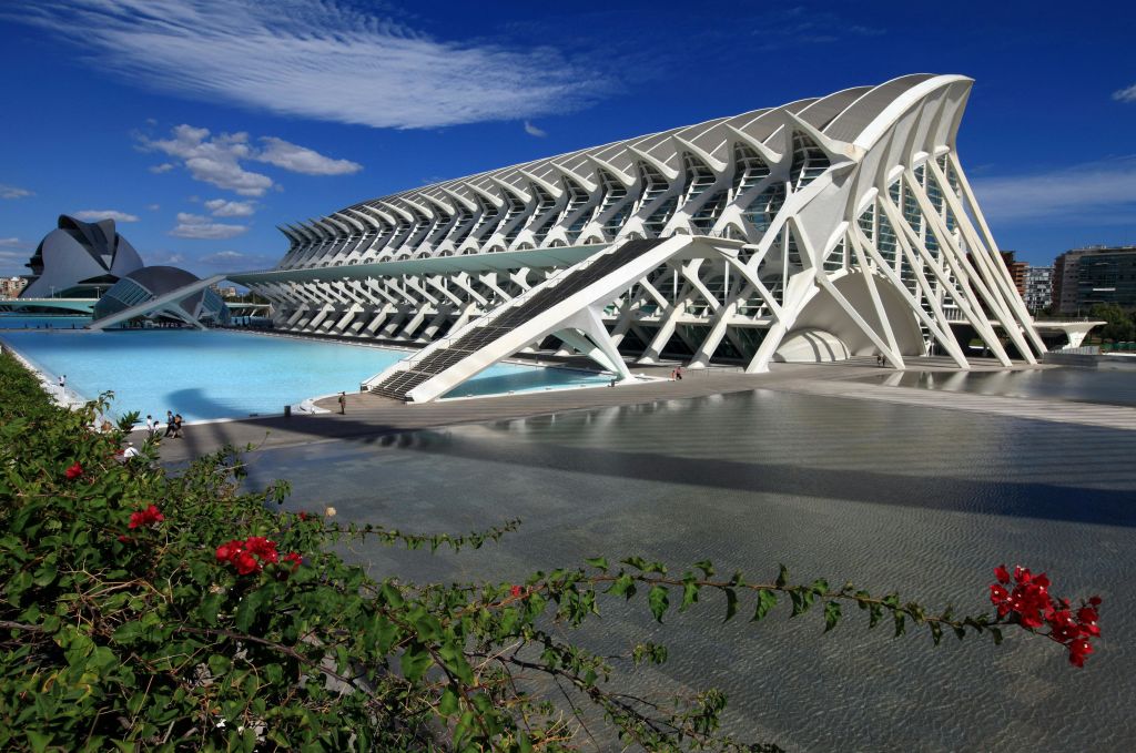 푸른 하늘을 배경으로 곡선형 디자인이 돋보이는 미래 지향적인 흰색 건축물. 전경에 수영장과 녹지가 반사됩니다.